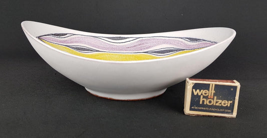 a white bowl with a colorful design on it, placed next to a matchbox labeled "well-holzer".
