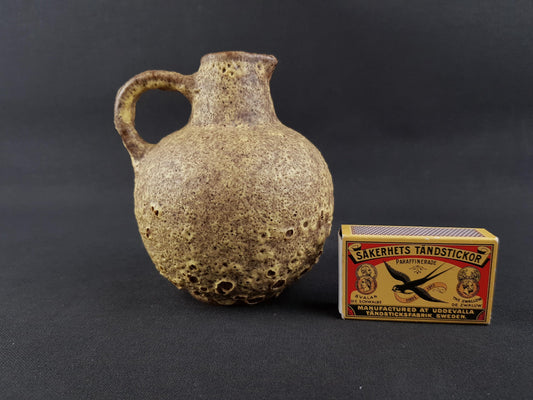 A ceramic vase and a matchbox are placed on a dark background.