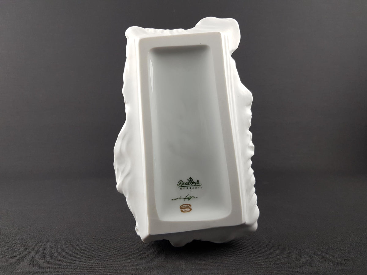 A white ceramic sculpture with a textured surface, featuring a logo and text at the bottom.
