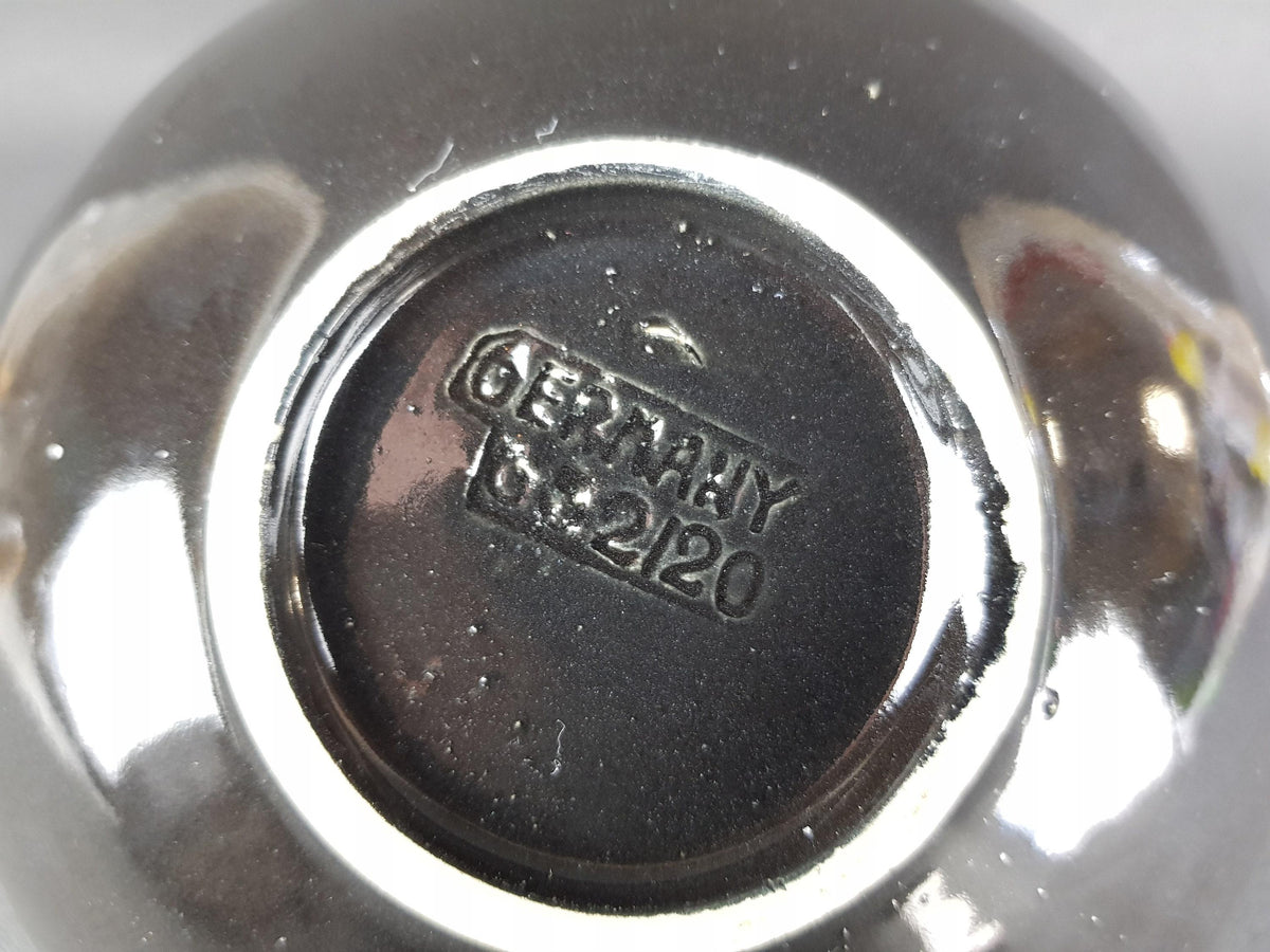 a close-up view of a metal object, possibly a bowl or a container, with a textured surface. The text engraved on the object appears to be in German and reads "GERMANY 2.120".