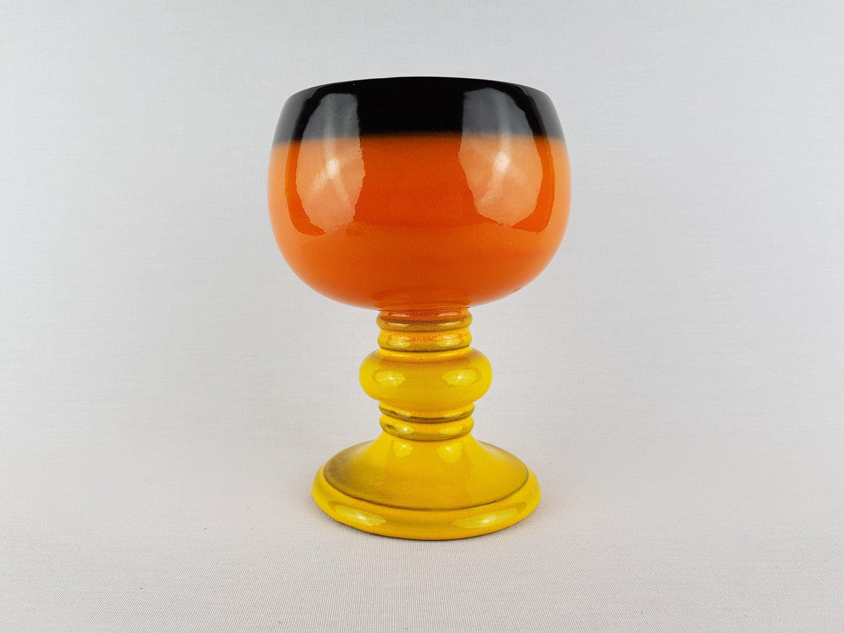a colorful glass vase with a black rim and a yellow base, placed on a white surface.