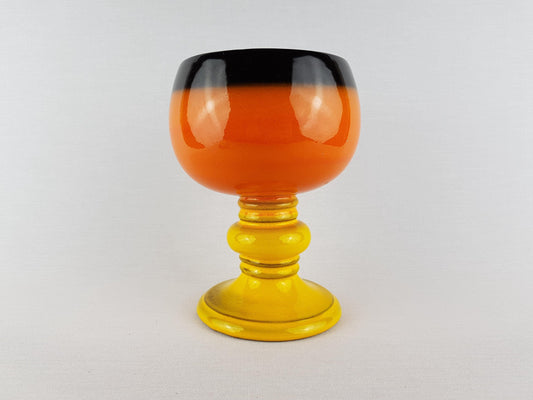 a colorful glass vase with a black rim and a yellow base, placed on a white surface.