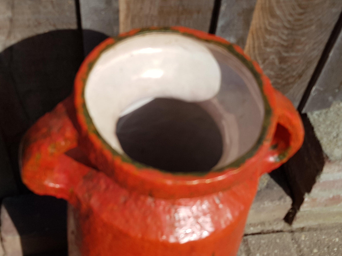 A red ceramic jar with a white interior, placed on a wooden surface against a wooden background.