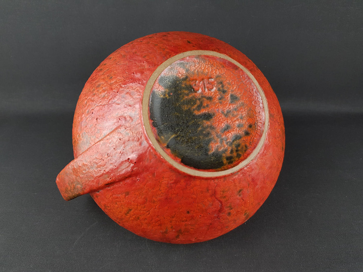A red ceramic bowl with a black rim and a small inscription on the back.