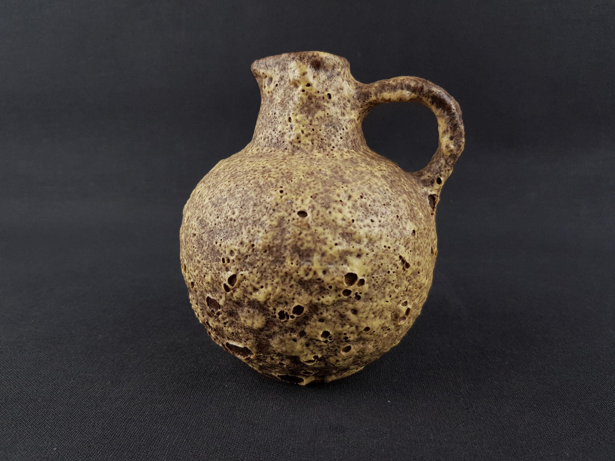 A ceramic vase with a handle, sitting on a dark background.