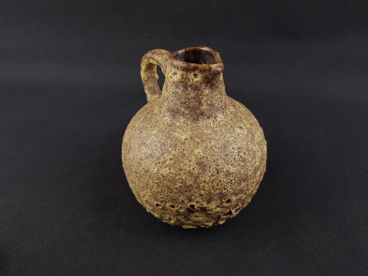 A ceramic vase with a brown speckled texture and a handle on the side, sitting on a dark background.