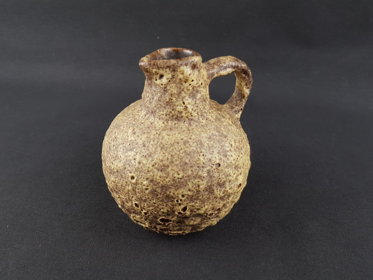 A ceramic pitcher with a handle, sitting on a dark surface.