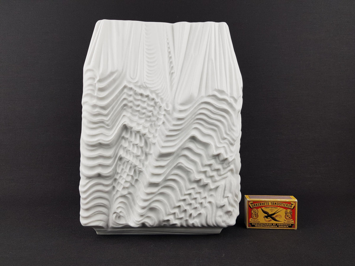a white, abstract sculpture with a textured, wave-like design, placed next to a matchbox.