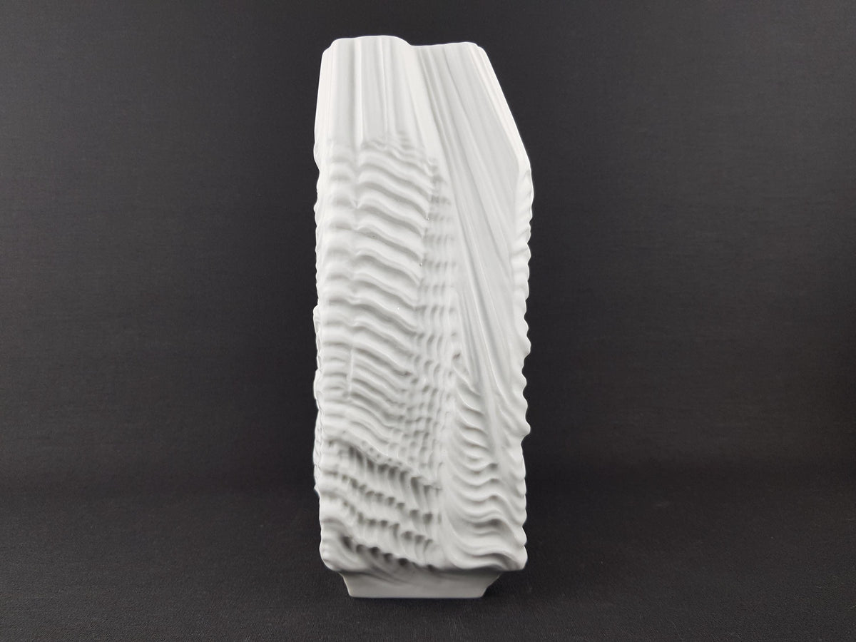 A white, abstract sculpture with a textured, wavy design stands against a dark background.