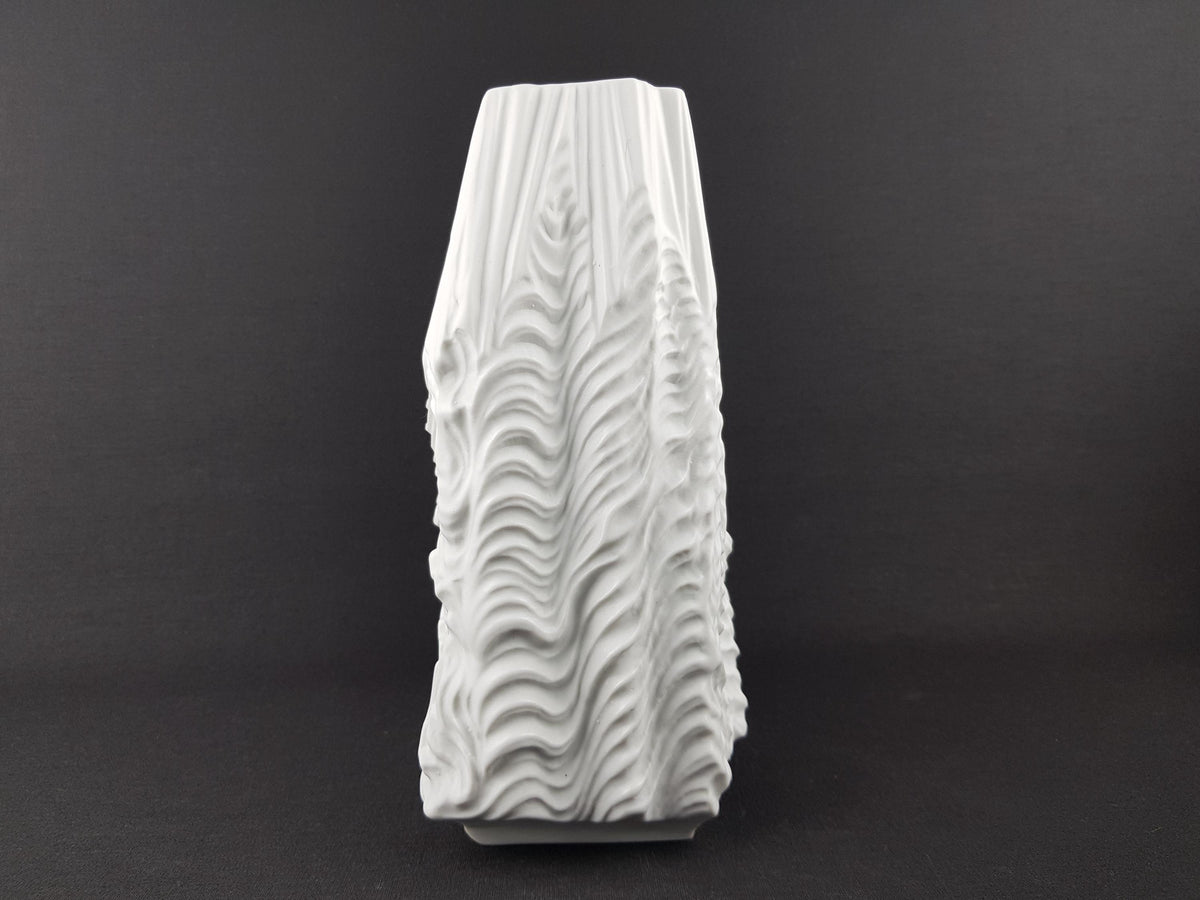 A white ceramic vase with a textured, wavy design on a dark background.