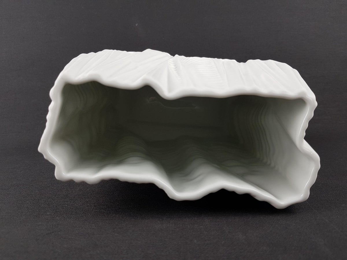 A white ceramic object with a textured, wavy surface is shown against a dark background.