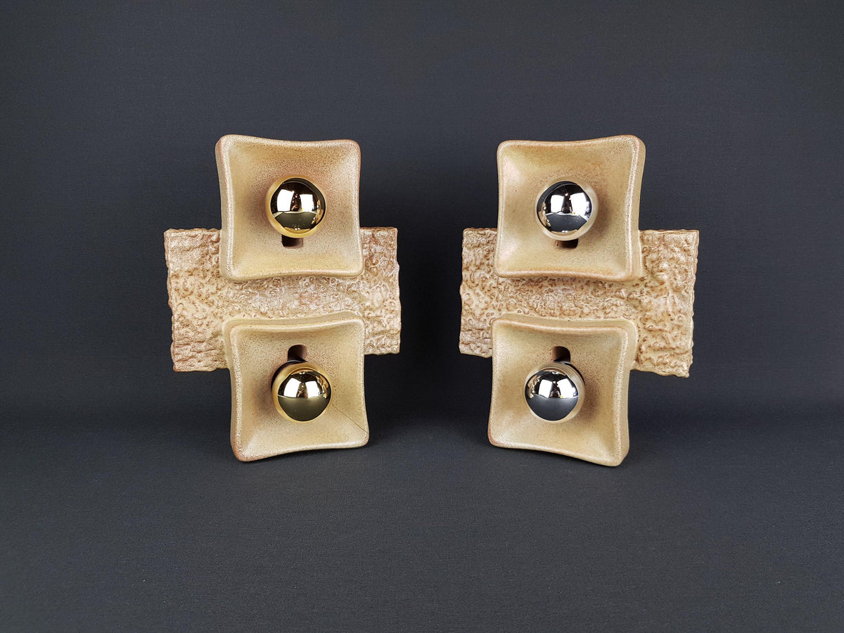 four square ceramic objects with a beige color and a metallic ball at the center, arranged in a symmetrical manner against a dark background.