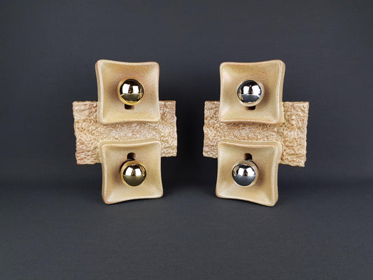 four square ceramic objects with a beige color and a metallic ball at the center, arranged in a symmetrical manner against a dark background.