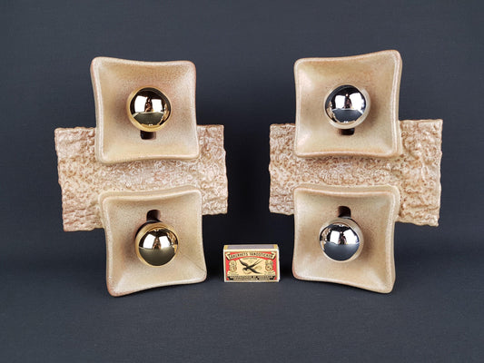 a collection of four ceramic objects, each with a metallic ball or orb attached to it, arranged in a square formation. There is also a small matchbox placed in front of the ceramic objects.