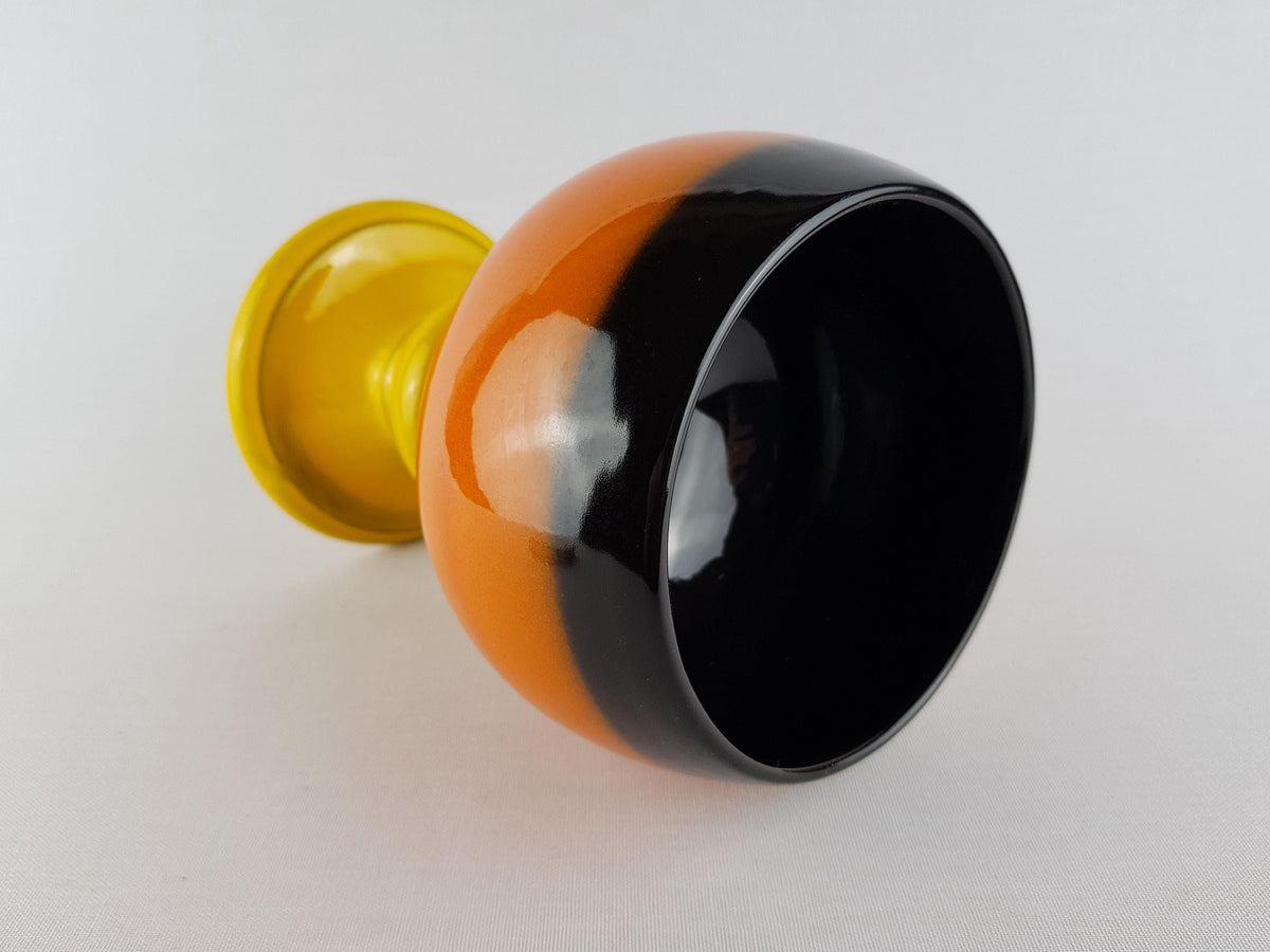 a black and orange vase with a yellow base, placed on a white surface.