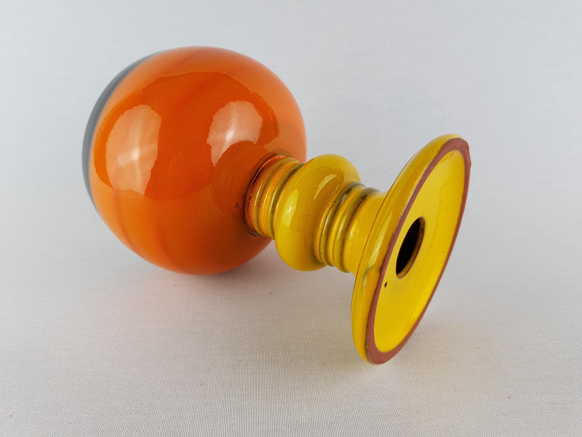 An orange and yellow glass vase with a yellow base and a black rim is shown against a white background.
