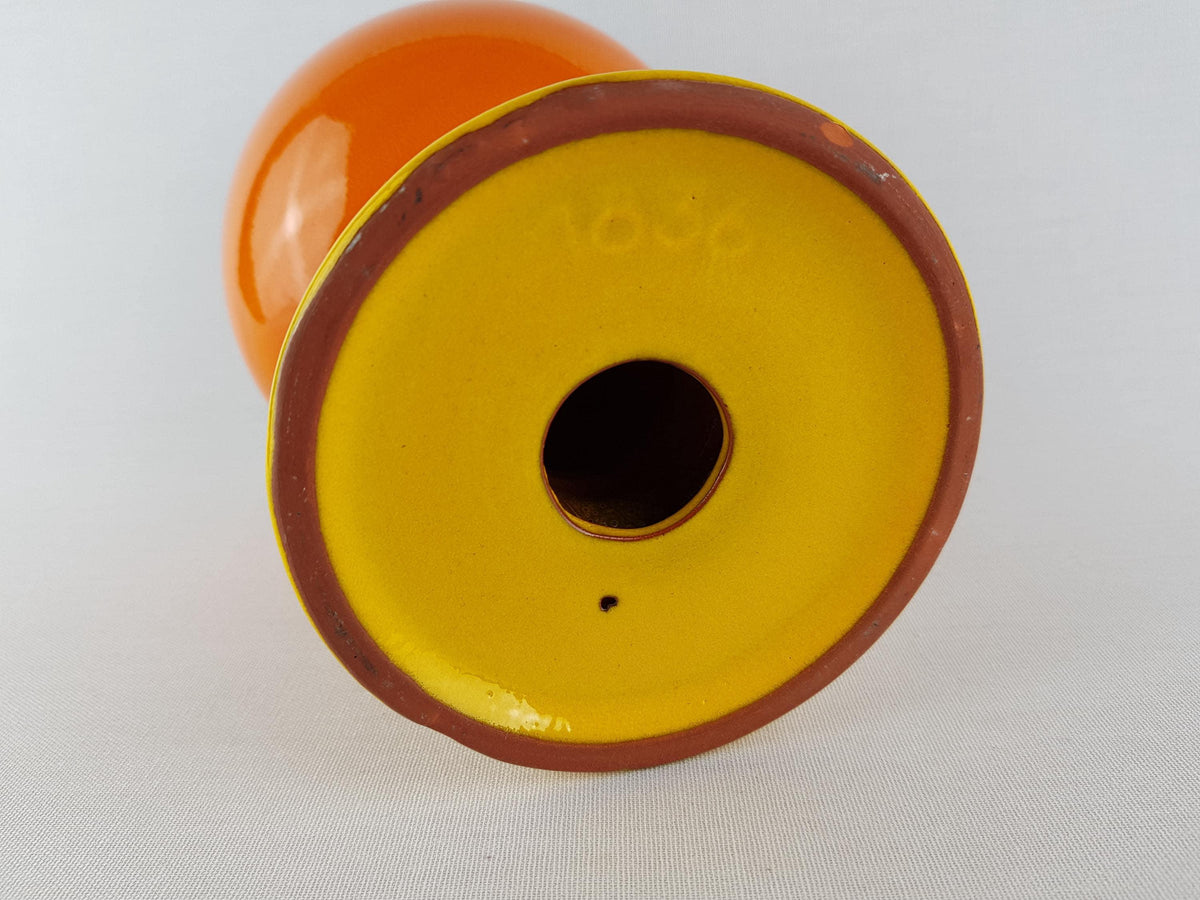 a close-up view of a yellow and orange ceramic object, possibly a vase or bowl, with a small hole in the center.