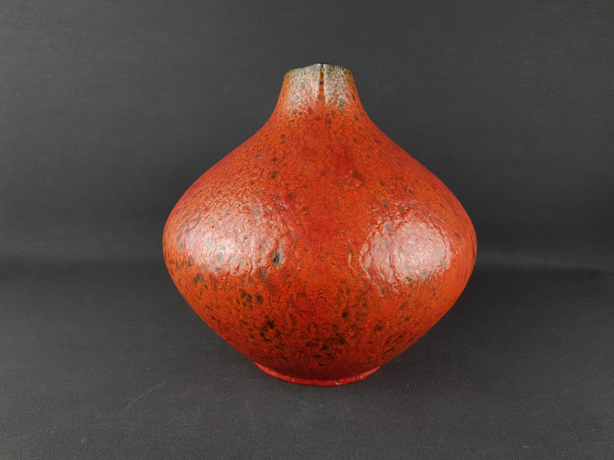 A red ceramic vase with a textured surface sits against a dark background.