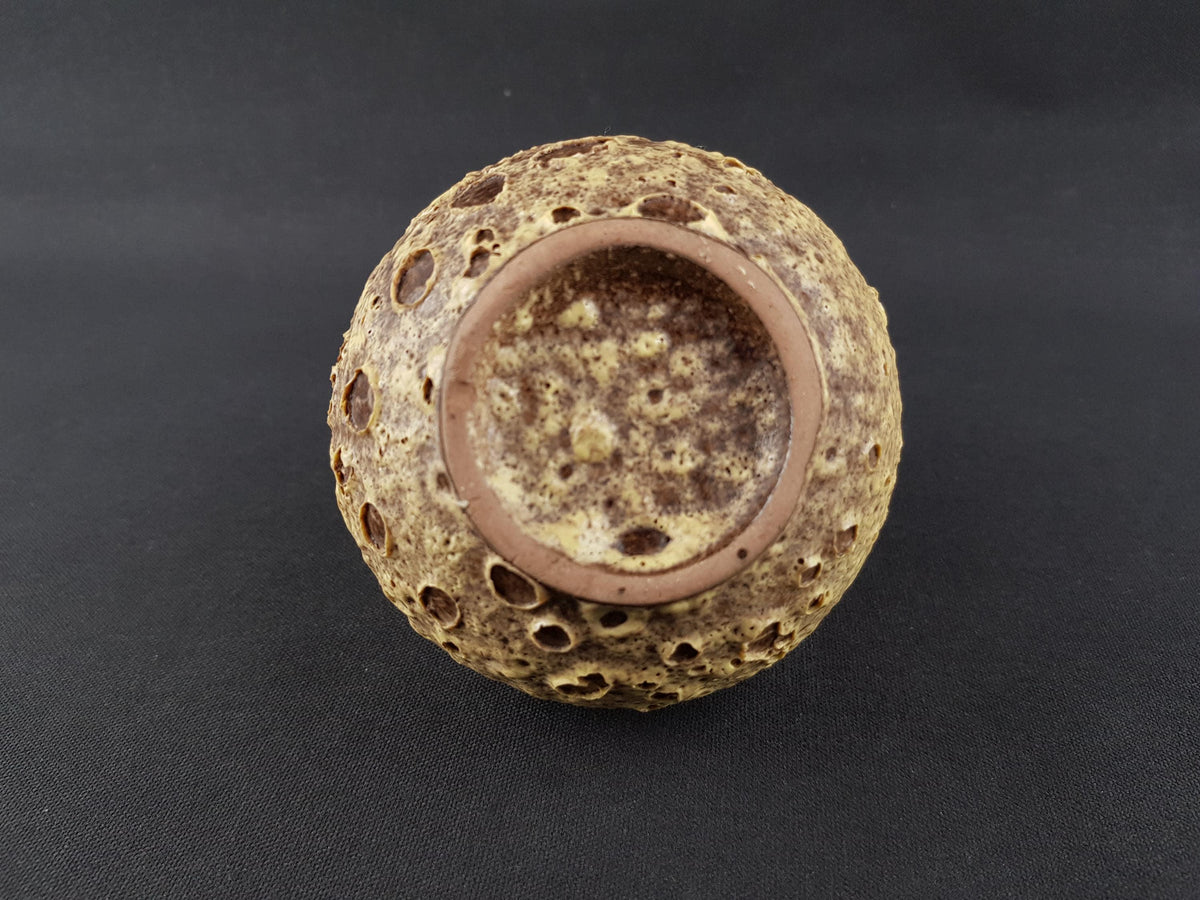 A brown, textured vase with a circular opening, sitting on a dark surface.